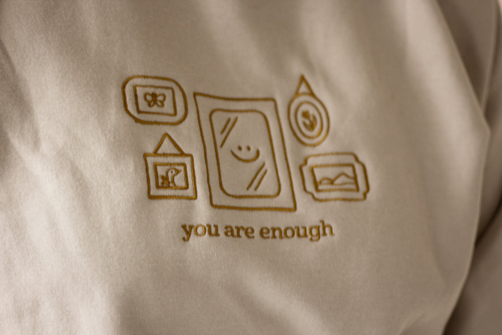 Beige fabric with brown embroidered design and 'you are enough' text